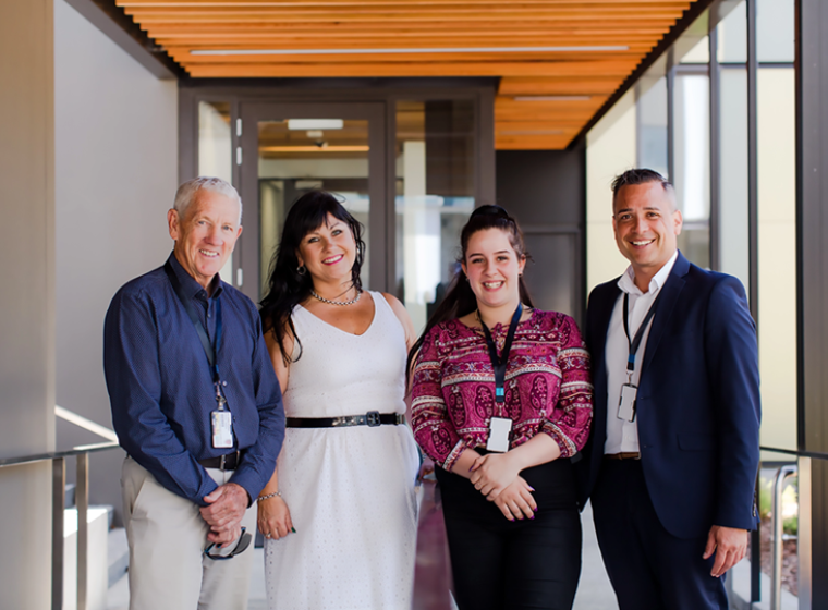 4 Health New Zealand office workers standing in a sunny walkway and smiling.
