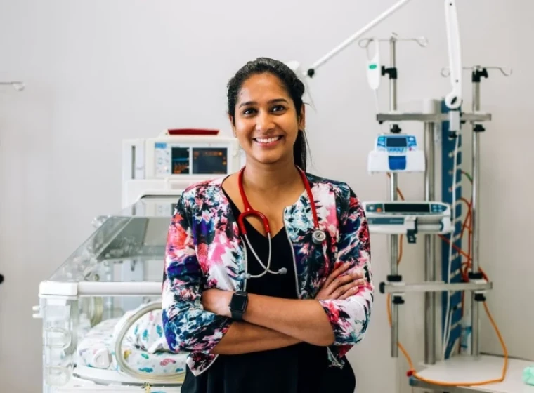 Krishna, a Resident Medical Officer stands smiling with her arms crossed in front of an incubator.